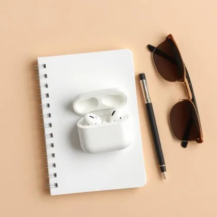 Top-down flat lay of the earbud case on a notebook with a pen and sunglasses — Flat Lay style, generated by ListIQ Pro