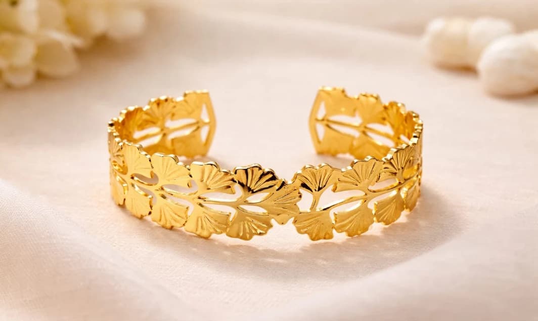 Original product photograph of a gold-plated leaf-pattern cuff bracelet on fabric, used as the input for AI video generation